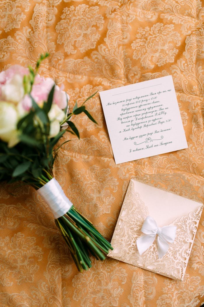 A flat lay of a bridal bouquet and wedding invitation on floral fabric, ideal for wedding themes.
